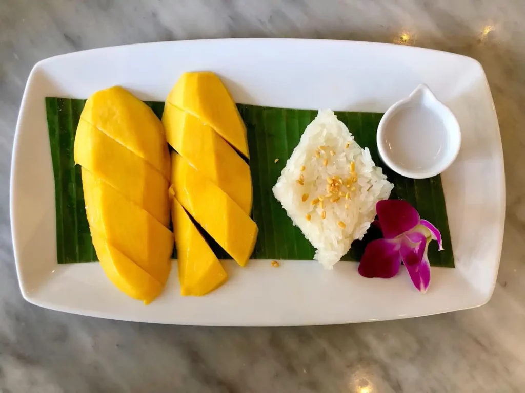 Mango mit Sticky-Reis mit Mungobohnen. Garniert mit einer Soße süßer Kondensmilch und dekoriert mit einer Lotusblüte