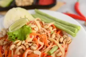 Thailändischer Papaya Salat auf weißem Teller geschmackvoll angerichtet und dekoriert
