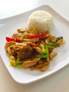 Thailändisches Gericht mit Ingwer und Hühnchen sowie Jasmin-Reis auf weißem quadratischem Teller angerichtet