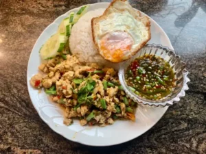 Pad Grapao - thailändisches Gericht mit Jasminreis und scharfer Soße sowie klein geschnittenem Hühnchenfleisch auf weißem runden Teller