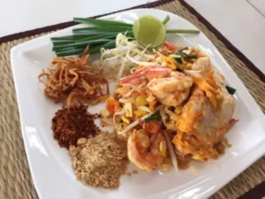 Thailändisches Gericht Pad Thai dekorativ angerichtet auf schönem weißen Teller mit Gewürzen, Fleisch und Gemüse