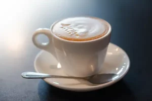 Cappuccino Kaffee mit Milchschaum in weißer Tasse mit Löffel auf schwarzem Hintergrund